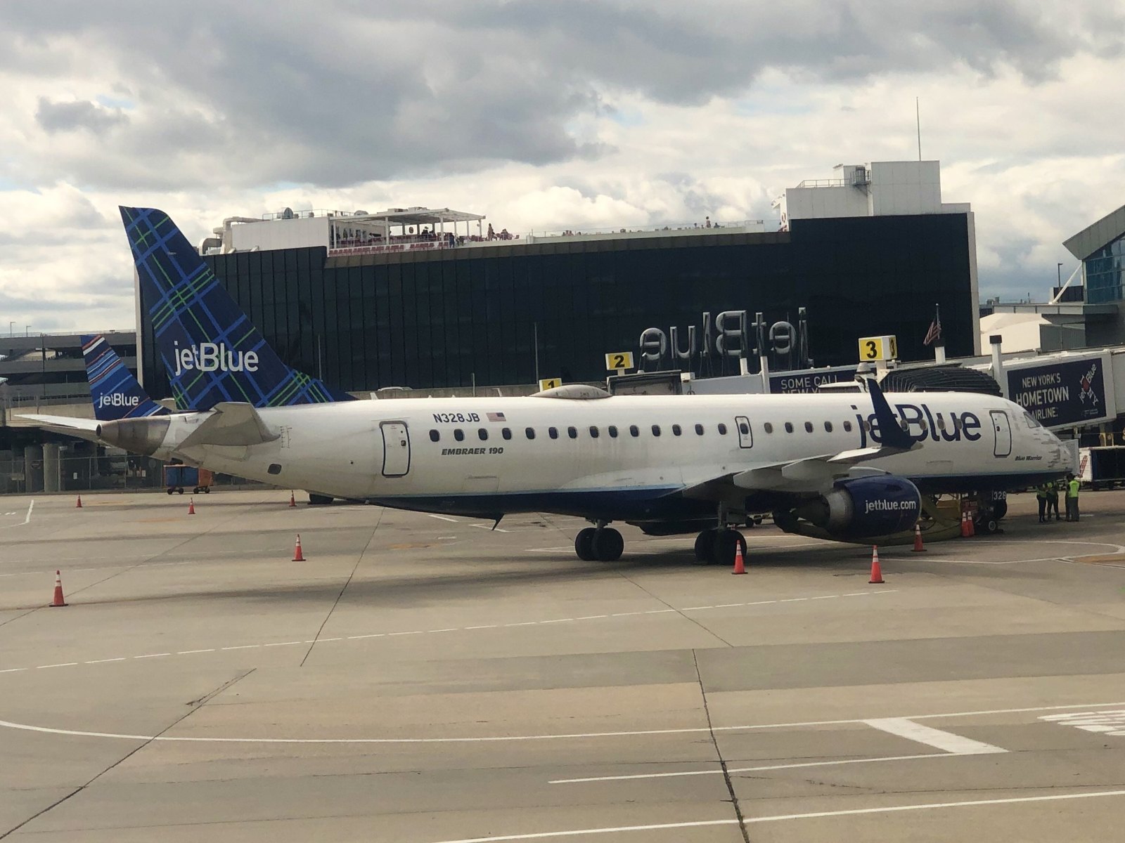 Photograph of a JetBlue Embraer E190 parked at a JFK gate with the jet bridge attached