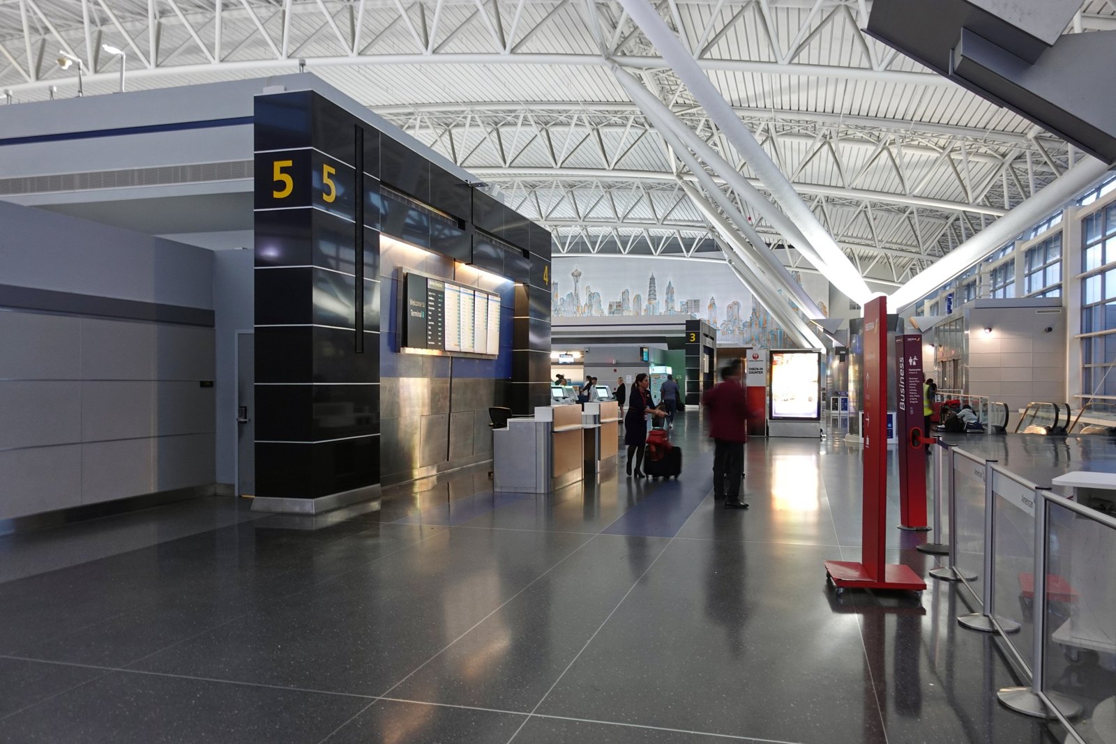 Interior photograph of a Terminal 8 concourse with seating, storefronts, and windows onto the apron